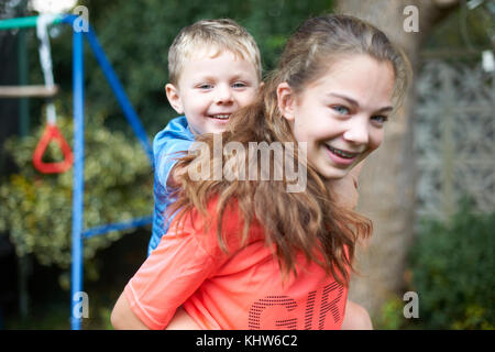 Portrait of young girl carrying young brother on back Stock Photo