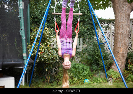 Young girl in garden, hanging upside-down from play frame Stock Photo