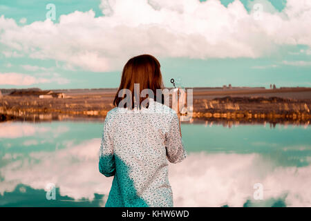 Woman blowing bubbles, cloudscape reflection in lake, Ural, Sverdlovsk, Russia Stock Photo