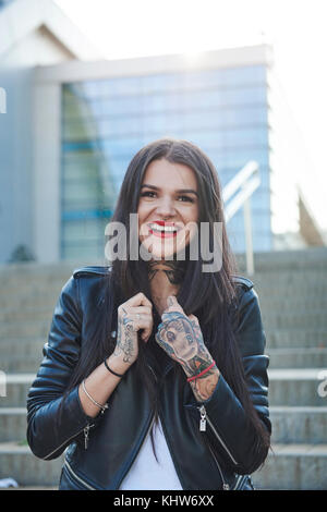 Portrait of young woman holding collars of jacket, smiling, tattoos on hands Stock Photo