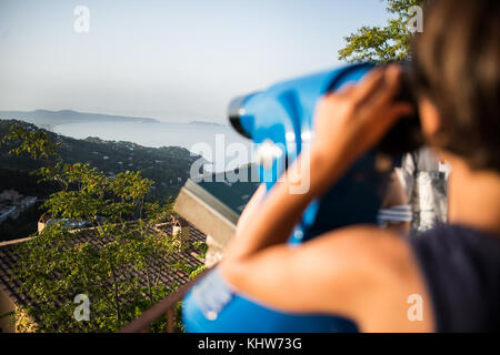 Over shoulder view of boy looking through coin operated binoculars at misty coastline landscape, Begur, Catalonia, Spain, Stock Photo