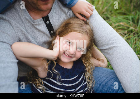 Father sitting with daughter on green grassy field Stock Photo