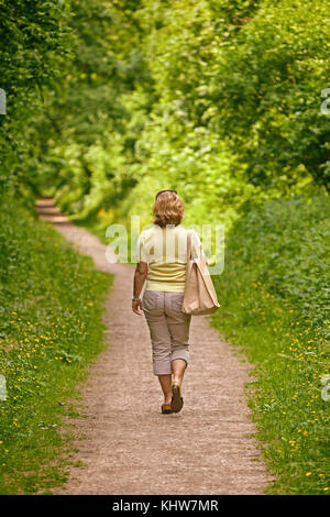 A woman walking down a footpath on a bright sunny day Stock Photo