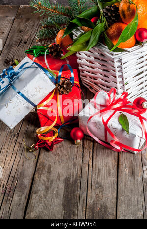 Christmas and New Year concept. Fresh Tangerines with green leaves in a white basket, Christmas decoration and gift boxes, on old rustic wooden table, Stock Photo