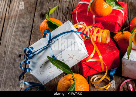 Christmas and New Year concept. Fresh Tangerines with green leaves in a white basket, Christmas decoration and gift boxes, on old rustic wooden table, Stock Photo