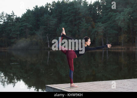 woman practicing yoga by a lake doing the dancers pose. Stock Photo