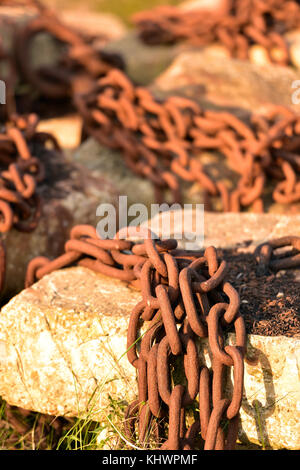 Some rusty and corroded old chains abandoned and left on some rocks on the seashore. Chains left out in the weather to rust. Stock Photo