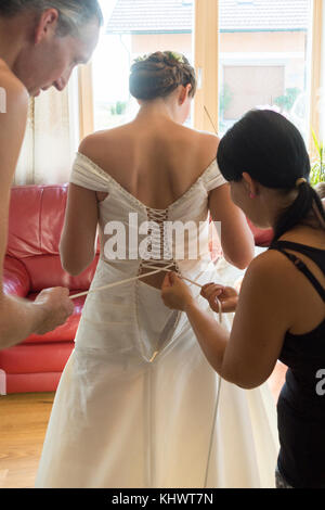 A young woman in her twenties being helped with her wedding dress by her father Stock Photo