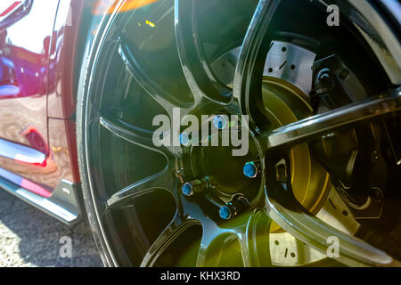 Black rims with blue bolt caps and red car door plus lens flare. Various tires at a southern California event. Stock Photo