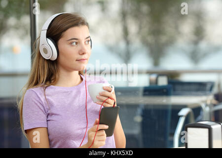 Serious teenager listening to music holding a coffee cup and a smart phone in a bar Stock Photo