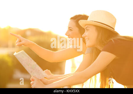 Side view portrait of two tourist friends pointing landmarks in an hotel balcony on vacations Stock Photo