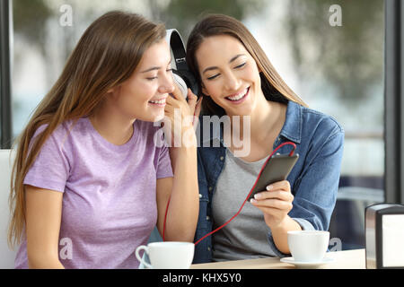 Two happy friends sharing on line music sitting in a bar