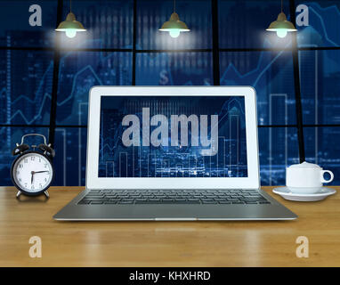 Workspace with computer laptop on the wood table which shown trading graph on the blurred photo of cityscape building background over the screen, trad Stock Photo