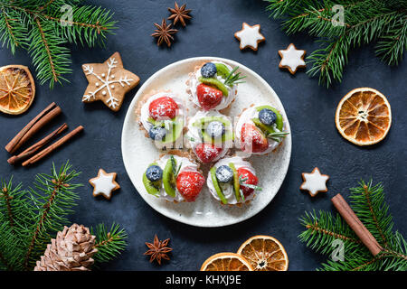 Christmas sweets, canape tartlets or cupcakes with cream and berries on white plate. Gingerbread cookies and festive decorations frame. Winter holiday Stock Photo