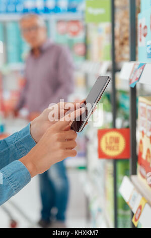 Woman shopping at the supermarket, she is checking products and offers using her smart phone, augmented reality and retail concept Stock Photo