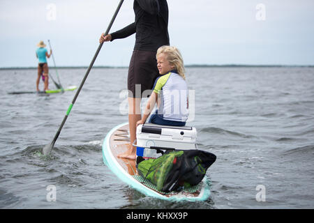 Woman on paddle board with young boy, another paddle boarder in distance Stock Photo