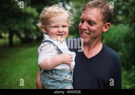 Portrait of man carrying toddler son, pulling a face Stock Photo