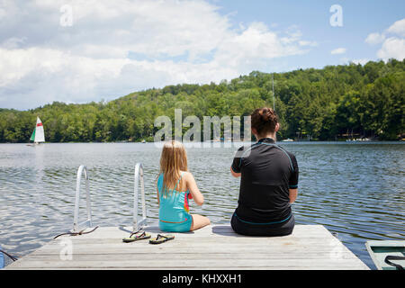 Two young girls sitting on jetty, rear view Stock Photo