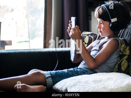Boy sitting on sofa listening to headphones and staring at digital tablet Stock Photo