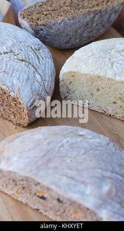 Vertical shot of different types of healthy, organic breads: brown, white, with nuts and seeds, cut in half, displayed on a wooden board Stock Photo