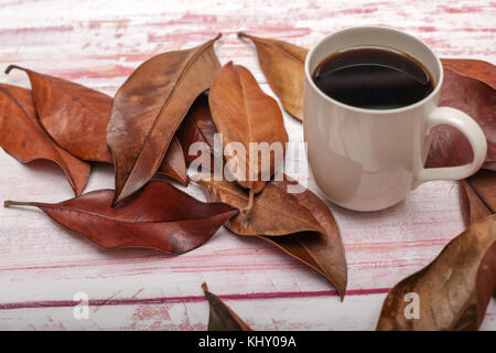 High angle view of a mug of coffee with autumn leaves on rustic wooden background Stock Photo