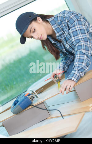 female carpenter measuring suitable wood board in workshop Stock Photo