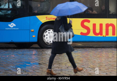 Muenster, Germany. 21st Nov, 2017. A pedestrian holding an umbrella crosses the street in Muenster, Germany, 21 November 2017. A bus shows an advertisement for holiday in the sun in the background. Credit: Friso Gentsch/dpa/Alamy Live News Stock Photo