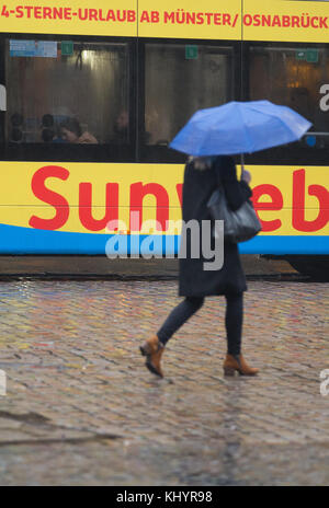 Muenster, Germany. 21st Nov, 2017. A pedestrian holding an umbrella crosses the street in Muenster, Germany, 21 November 2017. A bus shows an advertisement for holiday in the sun in the background. Credit: Friso Gentsch/dpa/Alamy Live News Stock Photo