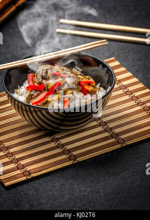 Asian rice with beef in black plate with chopsticks on dark stone table Stock Photo