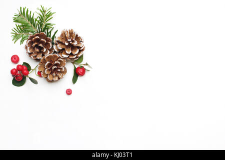 Christmas festive styled stock image floral composition. Pine cones, fir tree branches and red gaultheria berries on white wooden background. Flat lay, top view with empty copy space. Stock Photo