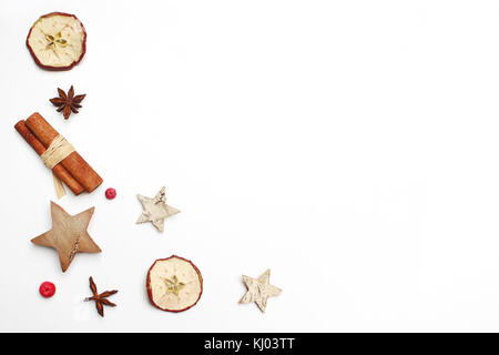 Christmas festive styled stock image composition. Decorative pattern. Cinnamon sticks, red berries, dried apple fruit, anise and wooden stars isolated on white wooden background. Flat lay, top view. Stock Photo
