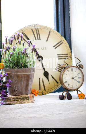 Still life of lavender plant, vintage clock face and alarm clock on windowsill Stock Photo