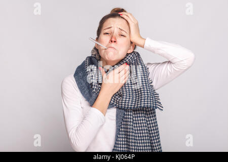 Young sick woman holding throat and head. Have a temperature. Studio shot, isolated on gray background Stock Photo