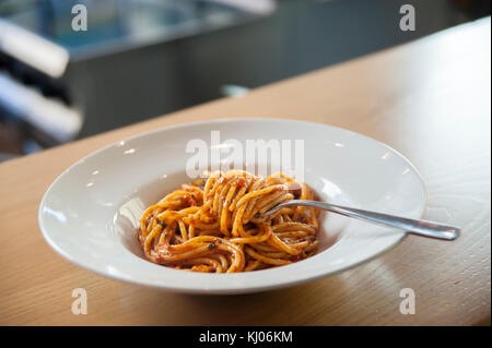 spaghetti in tomato sauce with fork, white ceramic plate on wooden shelf Stock Photo