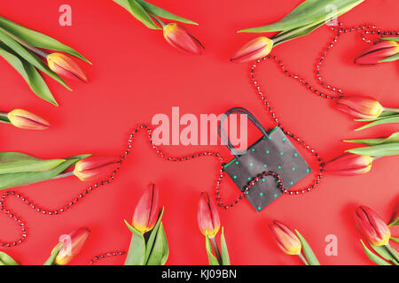 Gift, sale, shopping concept. Tulips composition with paper shopping bag on red background. Flat lay, top view Stock Photo