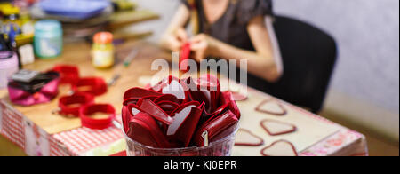 woman manufacturing heart-shaped red purses. purses are in focus. blurred background. Stock Photo