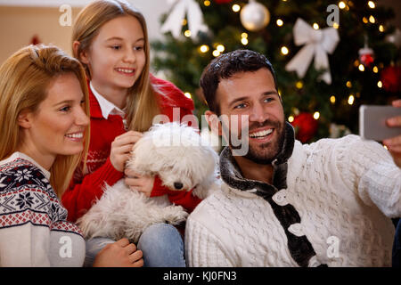 Parents with daughter and cute puppy making Christmas selfie Stock Photo