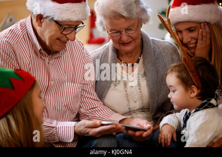 Happy grandparents with children looking Christmas photos on cell phone Stock Photo