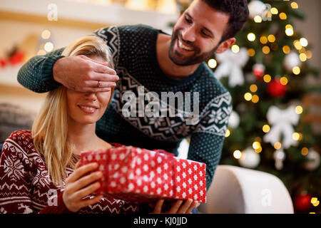Young man covering woman's eyes with hands and giving gift box Stock Photo