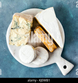 different kinds of italian cheese on a white marble cutting board . gorgonzola, goat, tomini and brie Stock Photo