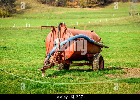 Tractor trailer tank for waste water or fertiliser manure. Industrial agriculture heavy machinery trailer is parked on a green meadow field in nature. Stock Photo