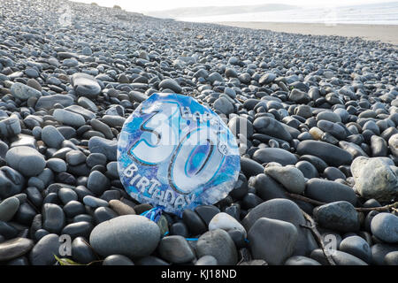 30th,Birthday,balloon,deflated,pollute,beach,found,on,pebbles,Ynyslas Beach,near Borth,north,of,Aberystwyth,Ceredigion,Mid,West,Wales,UK,U.K.,Europe, Stock Photo