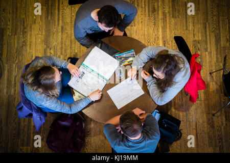 Higher education in the UK: An overhead view of a  group of four University students , two male two female, sitting around a table in a cafe refectory discussing work notes after or before a class lecture seminar tutorial Stock Photo