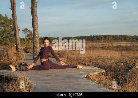 woman practicing yoga outside in open space in a nature reserve, doing the splits. Stock Photo