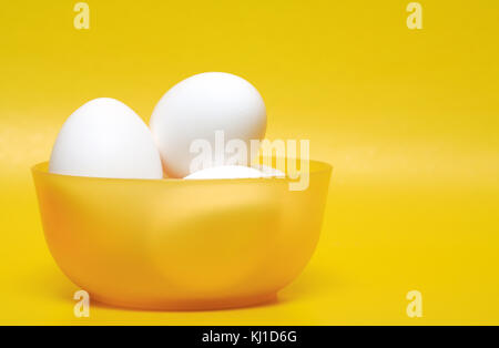Few white hen's eggs in plastic bowl on yellow background Stock Photo
