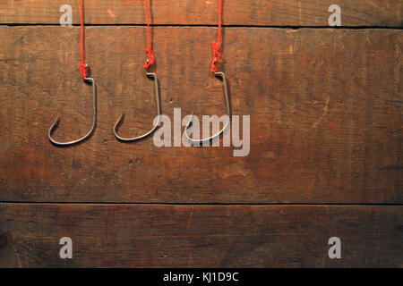 Three fishing hooks hanging with red ropes on wooden background Stock Photo
