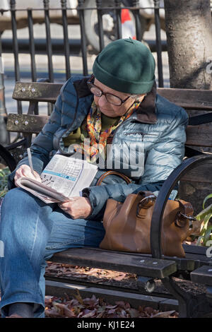 An older woman works on a newspaper crossword puzzle in Father Demo Park in Greenwich Village, Manhattan, New York City Stock Photo