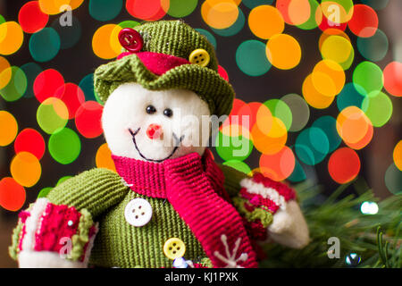 Toy snowman against festive Christmas lights in background Stock Photo