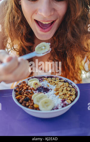 Young woman eating a acai in bowl, with banana, nut and tapioca. A typical tropical food. Stock Photo