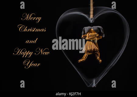 Christmas greetings with dancing straw dolls in a rotating metal heart and with the text: Merry Christmas and Happy New Year in straw/gold color Stock Photo